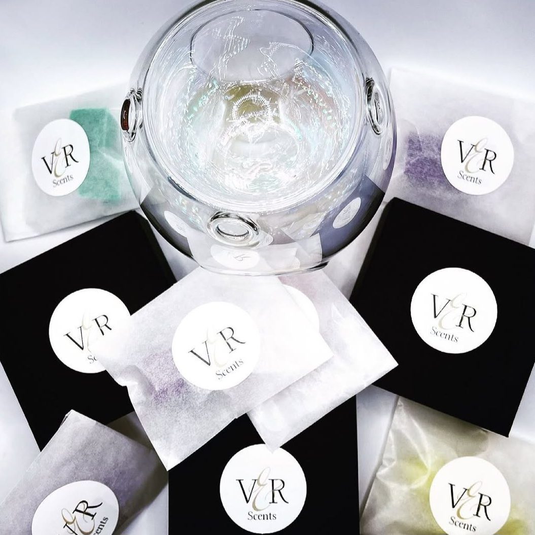 A glass wax burner surrounded by packets with "V&R Scents" branding on a white background.